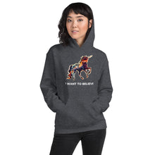 Load image into Gallery viewer, A woman with medium-length hair wearing a dark heather I Want To Believe Unisex Hoodie from Real Unicorn Apparel and a pair of fashionable pants. 
