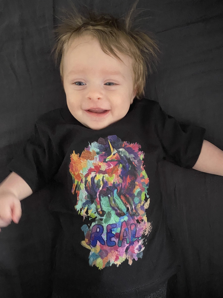 A photo of a blond-haired baby wearing a t-shirt with unicorn symbolism from Real Unicorn Apparel