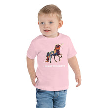 Load image into Gallery viewer, A young boy wearing a pink t-shirt from Real Unicorn Apparel&#39;s &quot;I Want To Believe&quot; collection. The shirt is designed for toddlers, has short sleeves, and prominently displays a rainbow-colored unicorn.
