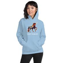 Load image into Gallery viewer, A chill-looking woman in a light blue hoodie from Real Unicorn Apparel&#39;s &quot;I Want To Believe&quot; collection. The hoodie has a rainbow-colored unicorn mid-gallop as its main design feature.
